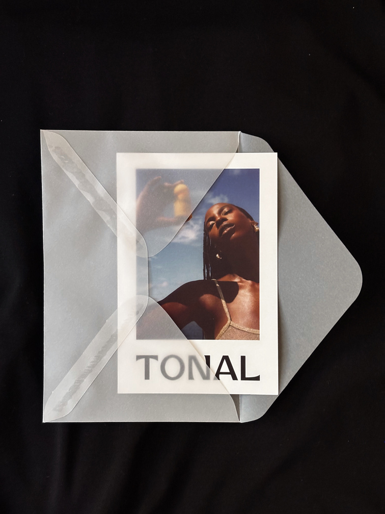 Partially open translucent envelope containing a card with a photo of a woman under blue sky and the word 'TONAL'.