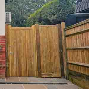 Double closeboard pedestrian gates beside red-brick house with paved path.