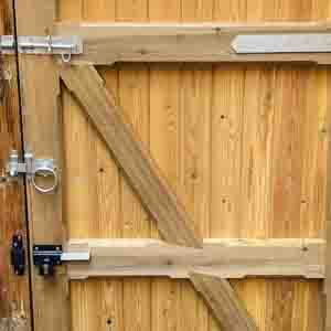 Natural timber gate with black hinges and top capping, installed beside brick wall.