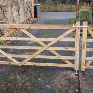 Five-bar timber entrance gate with diagonal bracing, installed at a rural driveway entrance.
