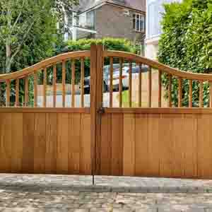 Framed timber entrance gates with arched tops and smooth finish, leading to a private driveway.