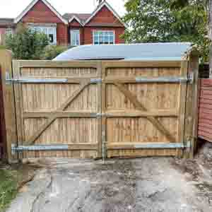 Natural timber driveway gates with framed design installed between brick piers.