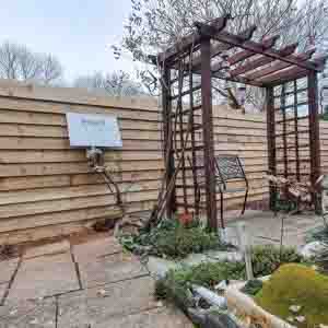 Decorative wooden pergola with climbing plants, installed beside a stone patio.