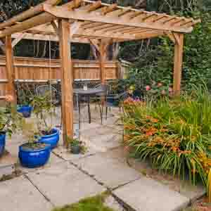 Wooden pergola structure built over a paved path with planters and garden seating.