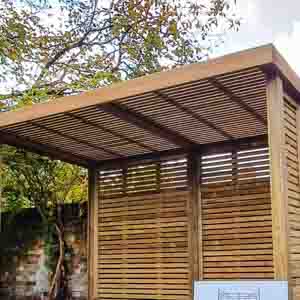 Wooden pergola providing shaded patio space beside a garden fence.