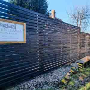 Modern black-painted slatted fencing installed beside a lawned garden.