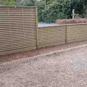 Long run of slatted fencing along a gravel driveway for privacy and style.
