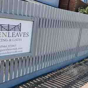 Painted picket fencing with Green Leaves Fencing & Gates signage along roadside.