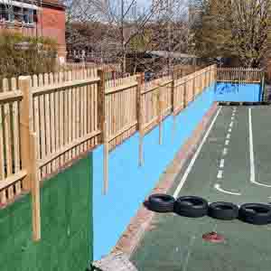 Picket fence with matching posts running beside a school playground and blue wall.