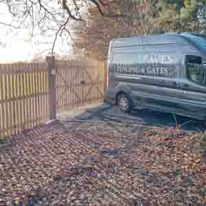 Picket fence enclosing a driveway with vehicle parked behind.