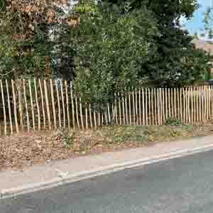 Natural timber picket fence running along a roadside verge beside hedging.