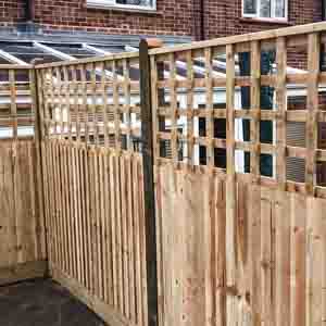 Fence line with staggered trellis panels and matching gate along a garden path.