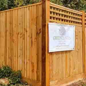Closeboard fence with square trellis detail above, set against shrubs.