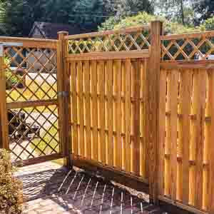 Trellis-topped fence run beside a paved path with potted plants.