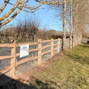 Long run of post and rail fencing following a gentle hill under blue skies.
