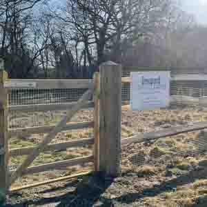 Timber post and rail fencing installed on sloping ground beside Green Leaves sign.