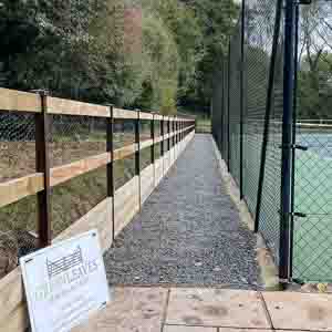 Post and rail fence running alongside a pond and pathway within a natural setting.