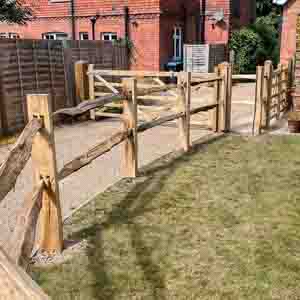 Chestnut post and rail fencing enclosing a front garden beside red brick houses.