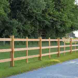 Straight run of post and rail fencing bordering a field next to a quiet country road.