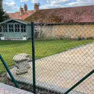 Green metal security fence protecting a tennis court in East Grinstead.