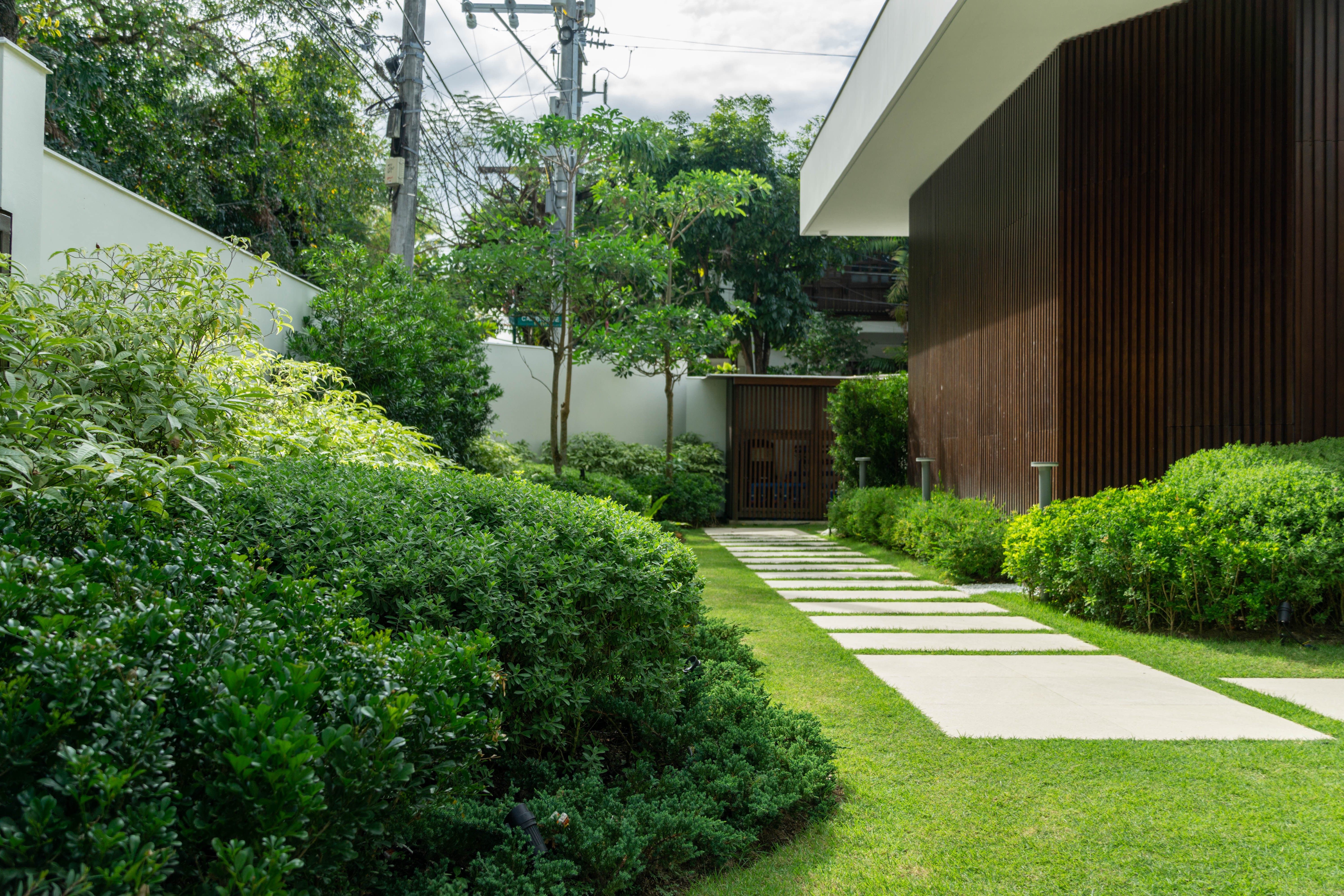 Bahay Huni — The garden pathway features stone step pads leading towards a wooden gate, surrounded by lush greenery and trees, offering a balance of manicured precision and organic growth