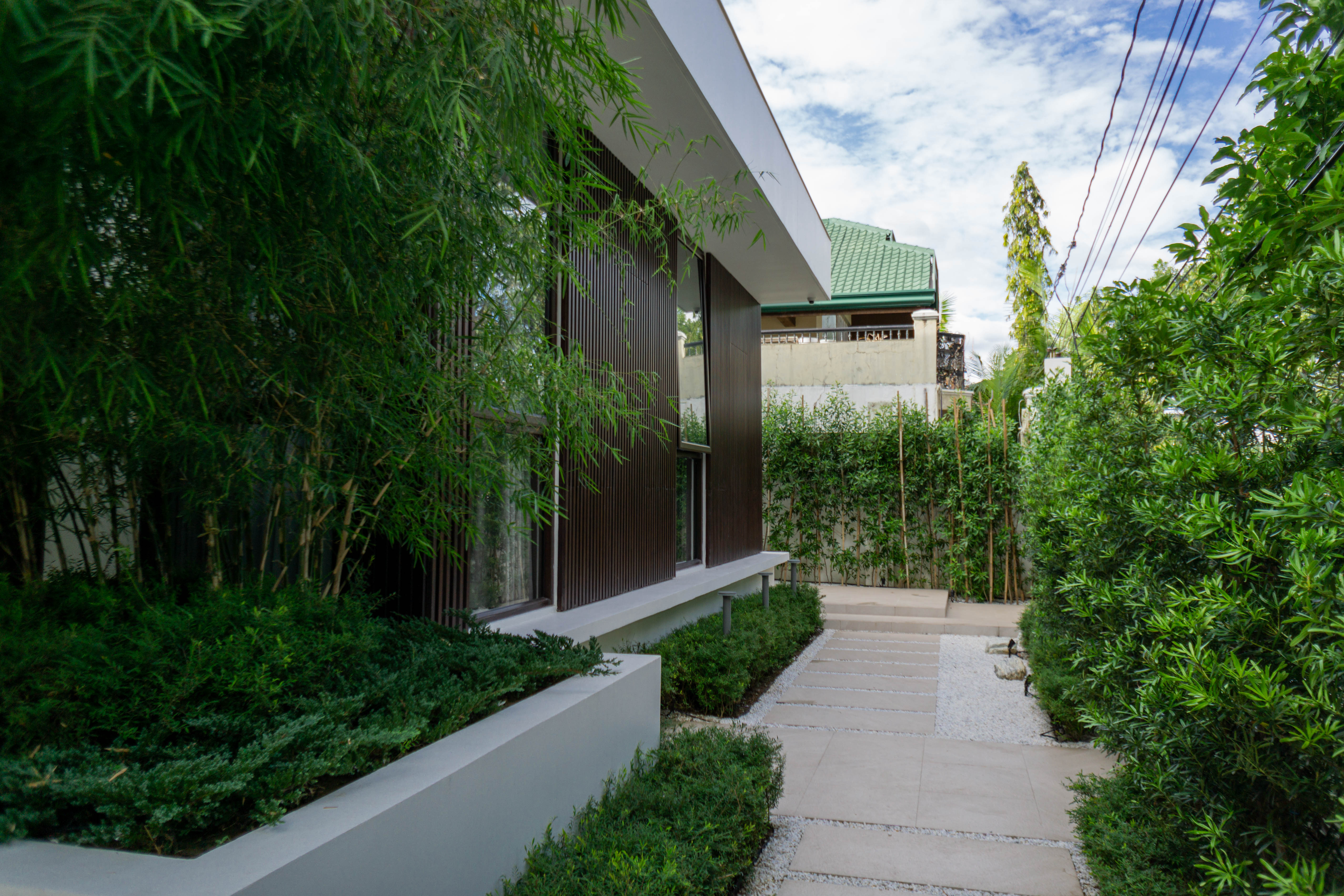 Bahay Huni — Vertical elements like plant boxes, green walls, and bamboo hedges offer a clever solution for this tight, challenging space, while the layered greenery and sleek pathway create a sense of openness