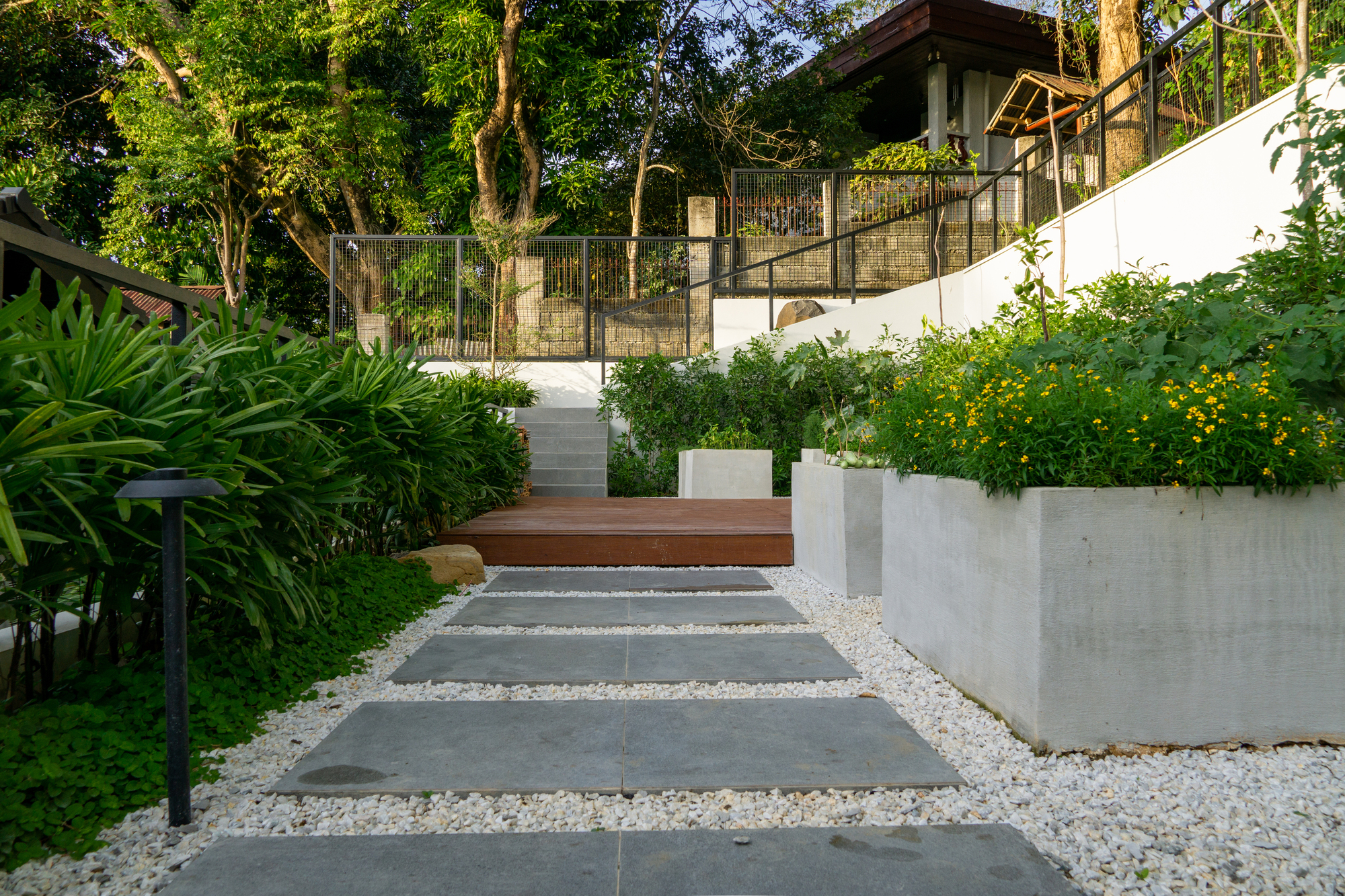 The Perch — A simple pebble pathway with raised planting beds and lush greenery greet guest and homeowner and lead them to a staircase that opens up to a massive green wall.