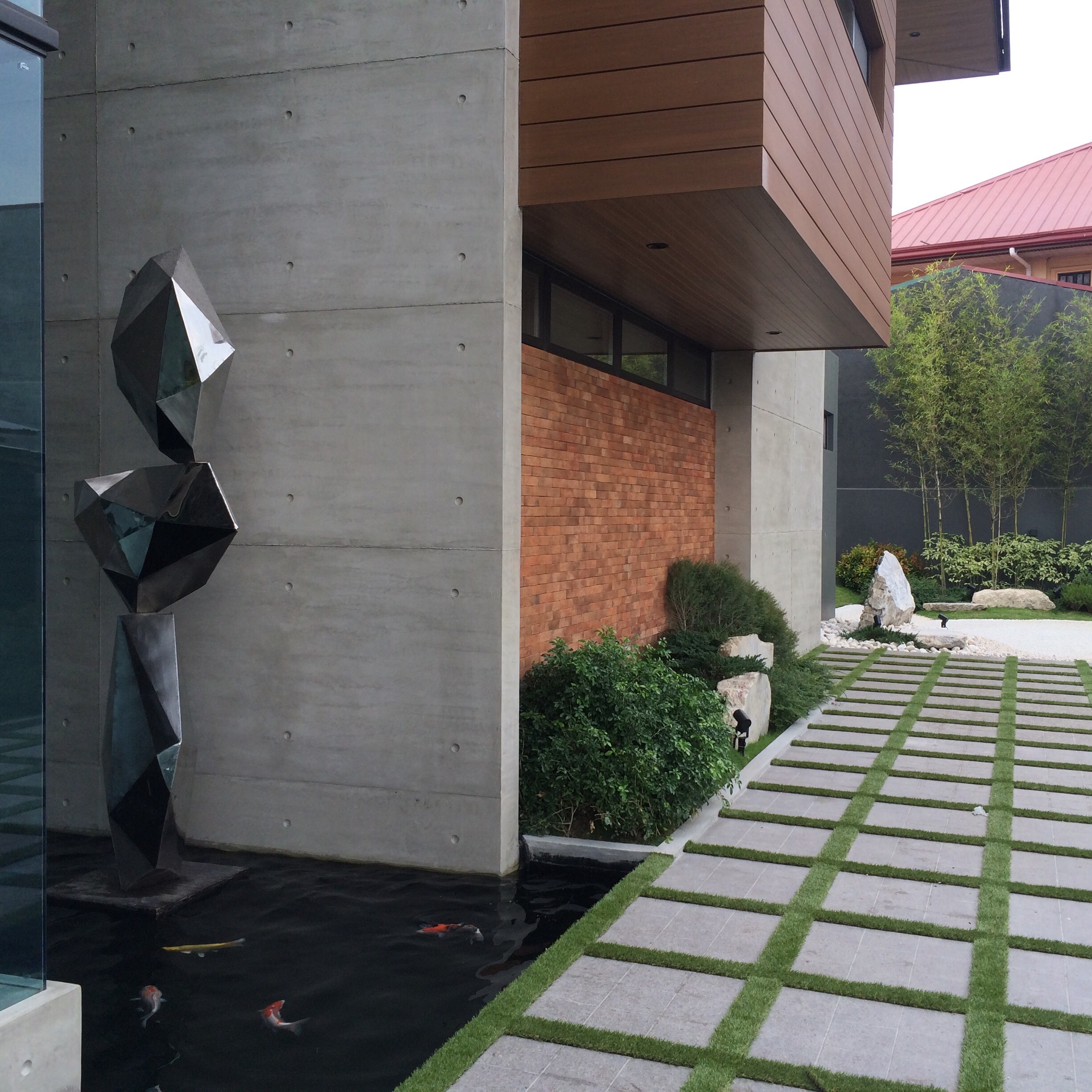 Walls of Green — The modern home, with its bold, monochromatic sculpture, and warm-toned materials, is complimented beautifully by the white tiles, boulder, lush plants and bamboos that surround and fill its spaces.