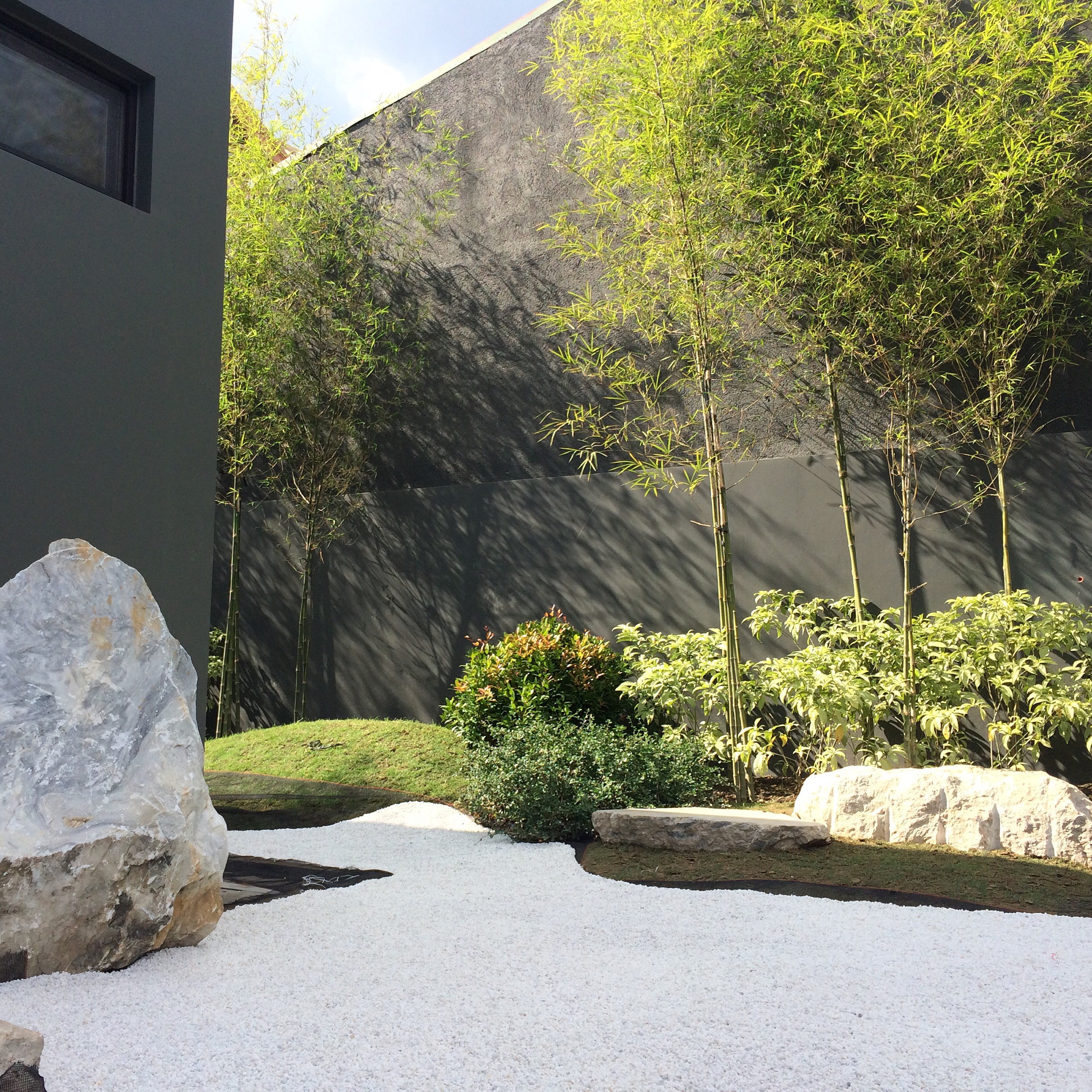 Walls of Green — Bamboos and finely-textured shrubs frame white gravel and boulders to brighten and contrast against the home's warm toned materials and its space.