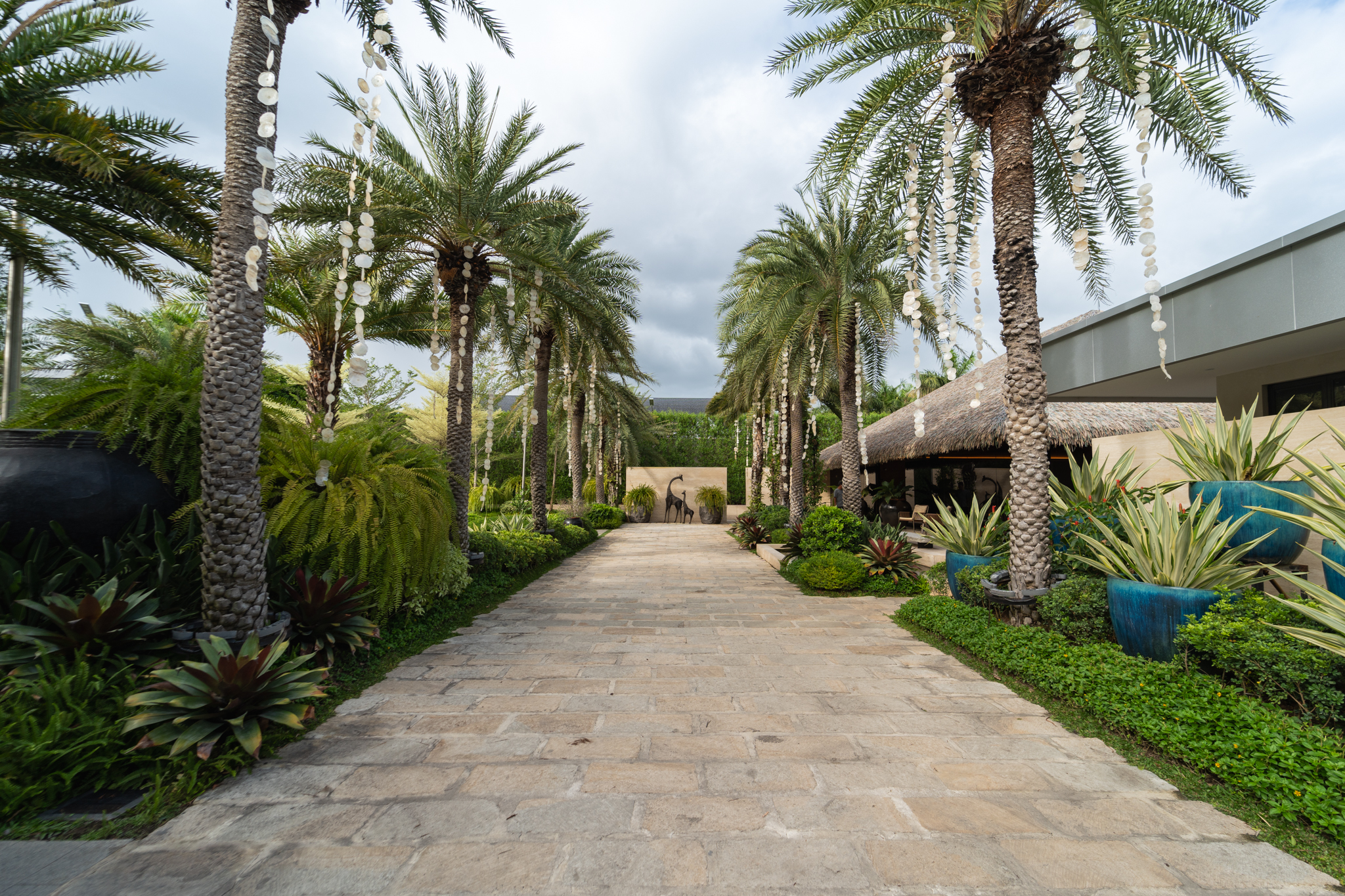 Lexus House — Palm trees, ferns, and other lush plants frame the stoned pathwalk to give off that tropical island feel perfect for a relaxing and peaceful outdoor getaway experience.