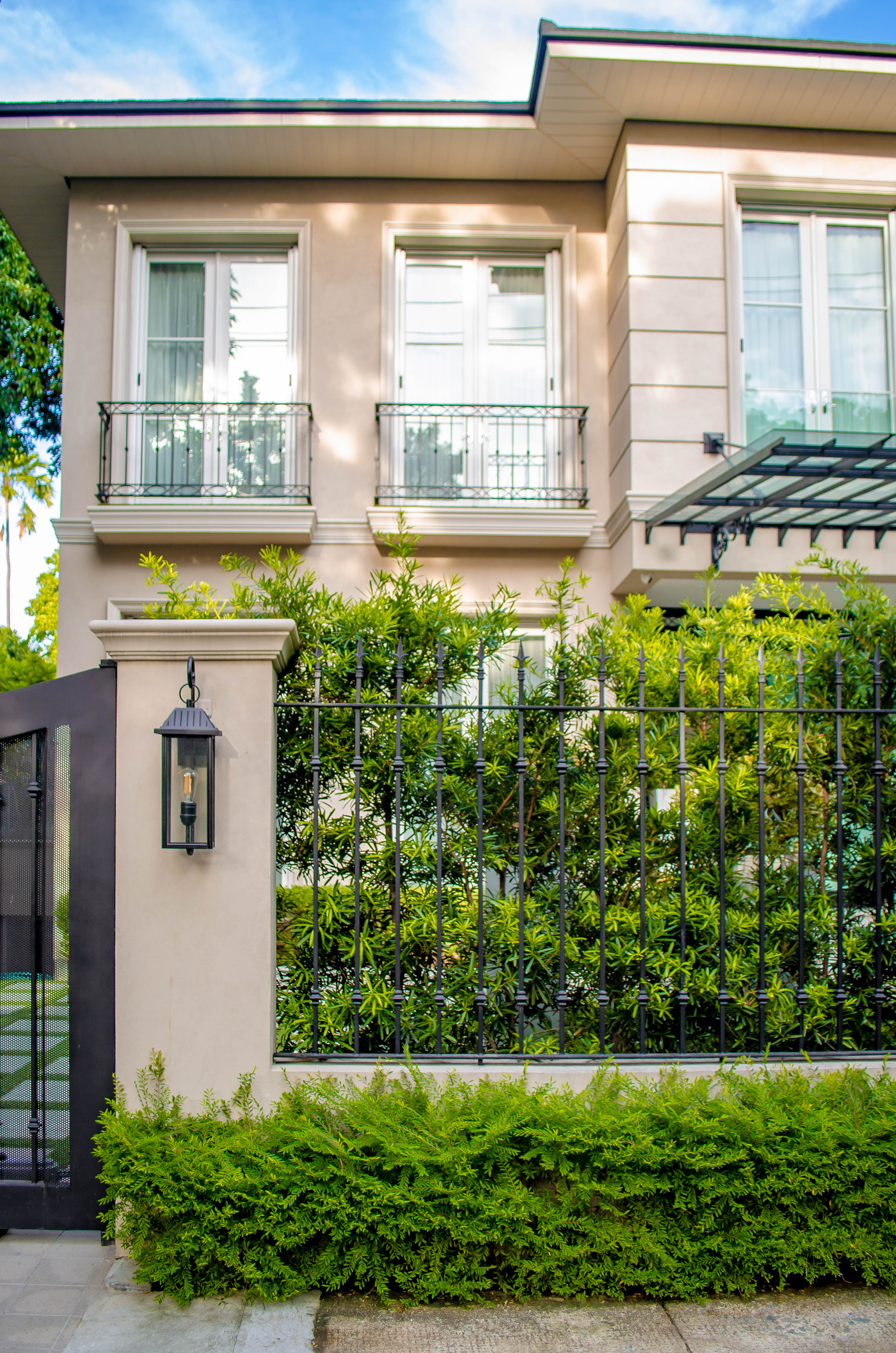 Formal French — A black fence sits in between trimmed bushes and a lush backdrop of plants, highlighting the natural beauty against the structured elements of the house.