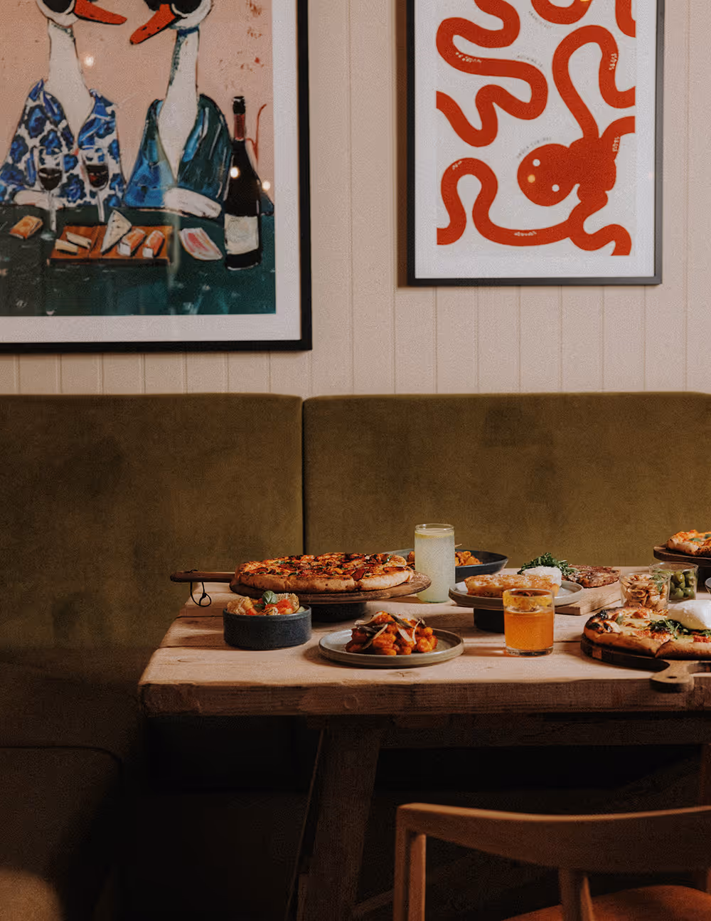 Table with pizzas, drinks, and appetizers in a cozy dining area with animal-themed wall art.