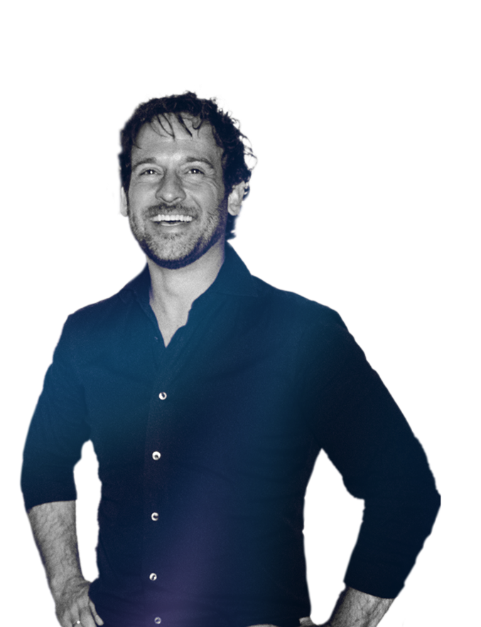 Smiling man with curly hair wearing a dark button-up shirt, standing with hands on hips.