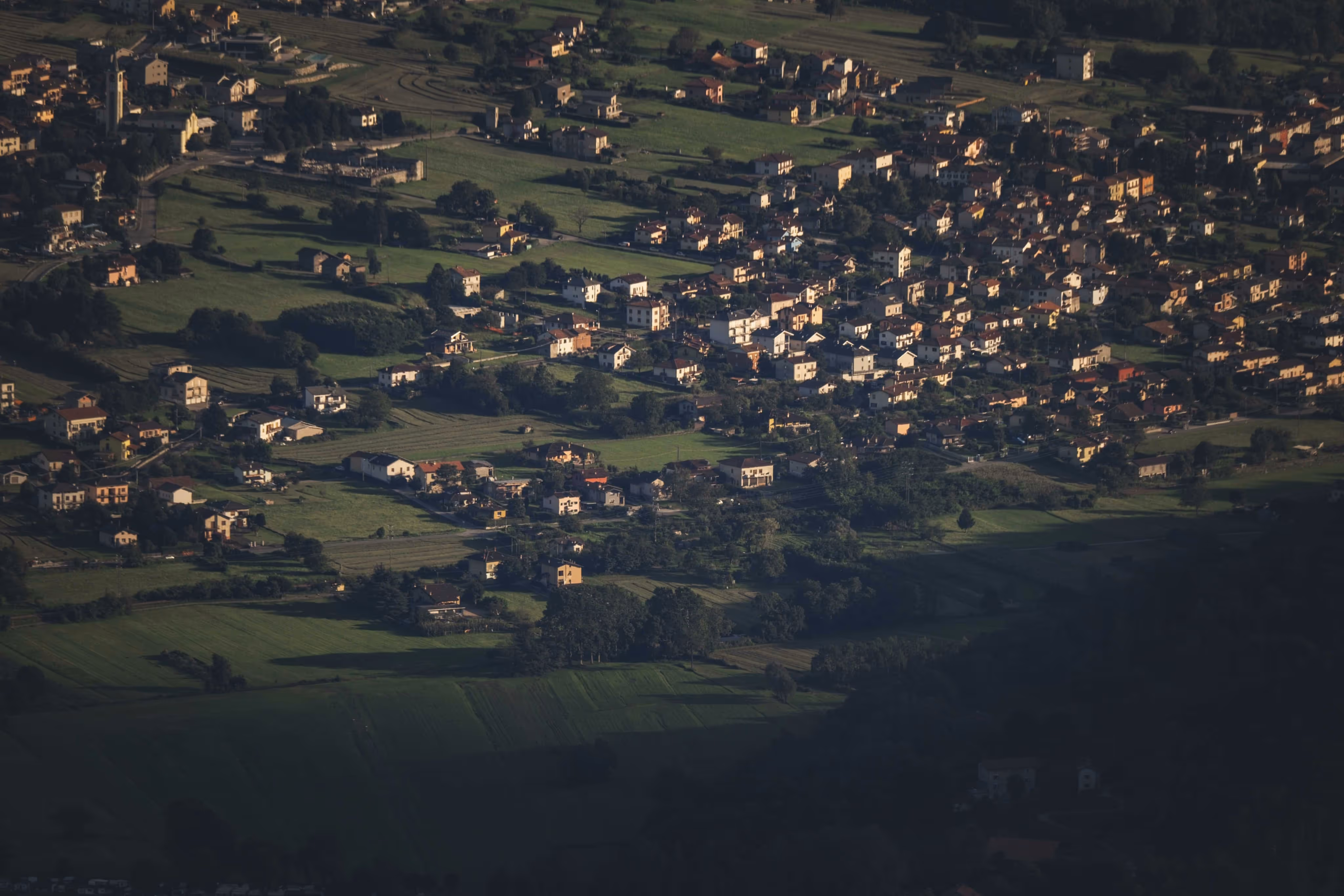 Vue aérienne d'une petite ville avec des maisons dispersées et des champs verts environnants.