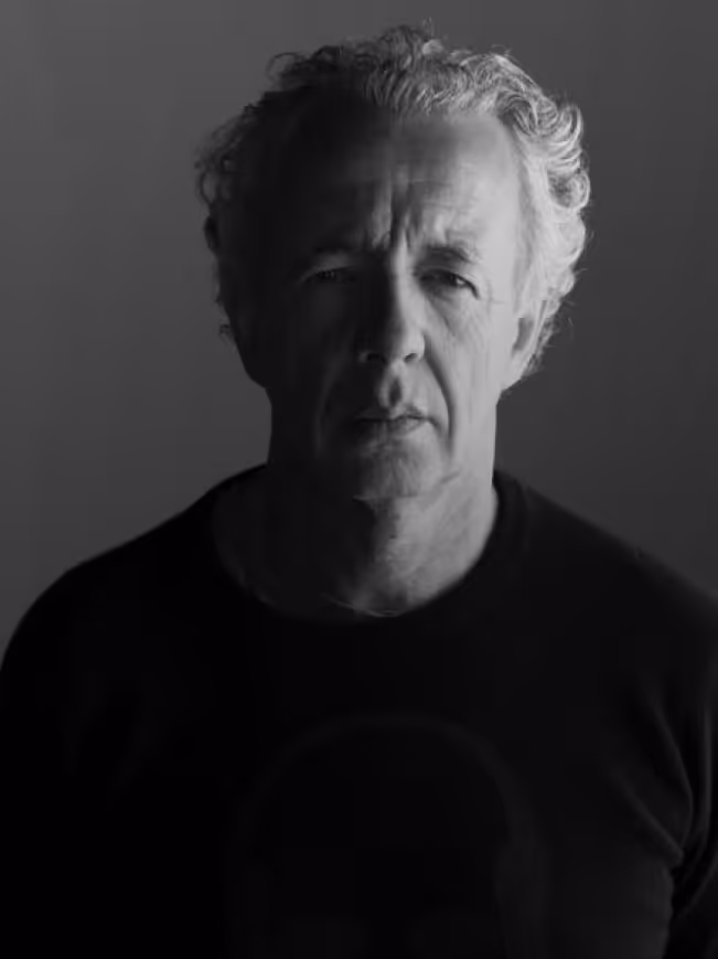 Black and white portrait of a middle-aged man with curly hair, wearing a dark shirt, looking directly at the camera.