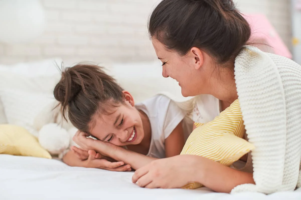 Mama și fiica râd și își spun reciproc povești, întinse pe pat.