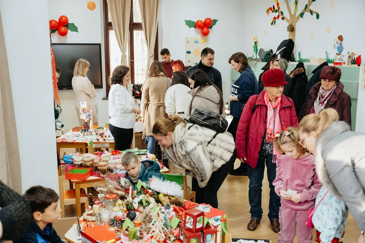 Szülők, nagyszülők és gyerekek válogatnak kézműves portékák között az óvoda adventi jótékonysági vásárán.
