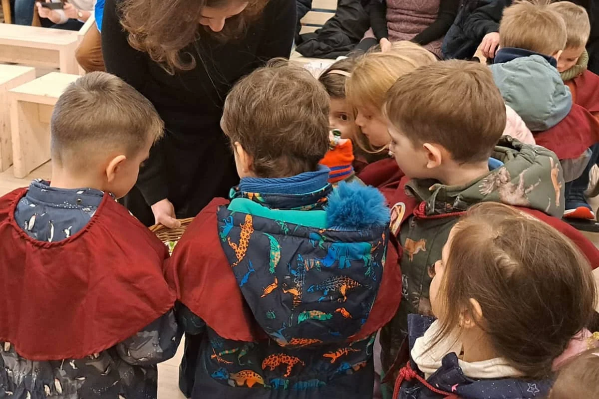 A hitoktató kosárból kínálja a gyerekeket a plébánián tartott kántáláson, ahol a gyerekek kíváncsian gyűlnek köré.