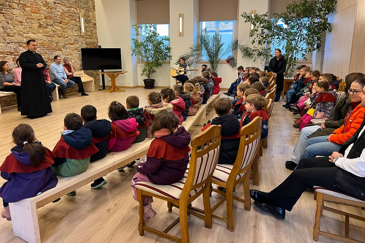 Copiii de grădiniță ascultă cu atenție cuvintele preotului în timpul colindatului de Crăciun