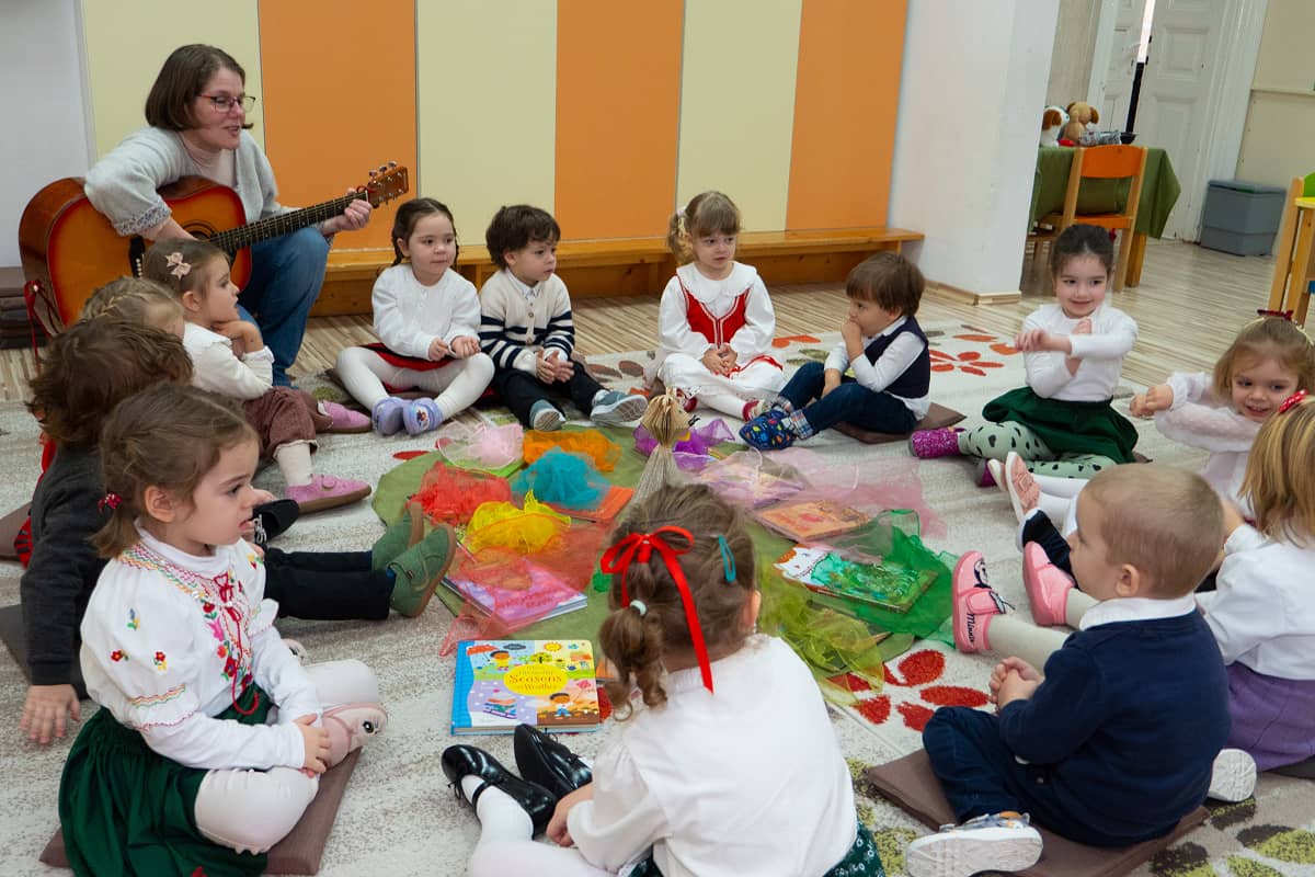 Activitate de cântec la grădiniță, cu acompaniament de chitară, într-o atmosferă festivă.