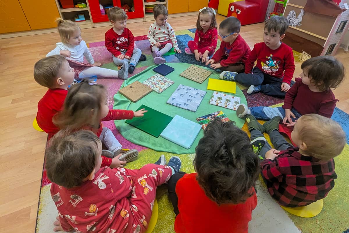 Bölcsődés gyermekek körben ülnek a becsomagolt könyvek körül.