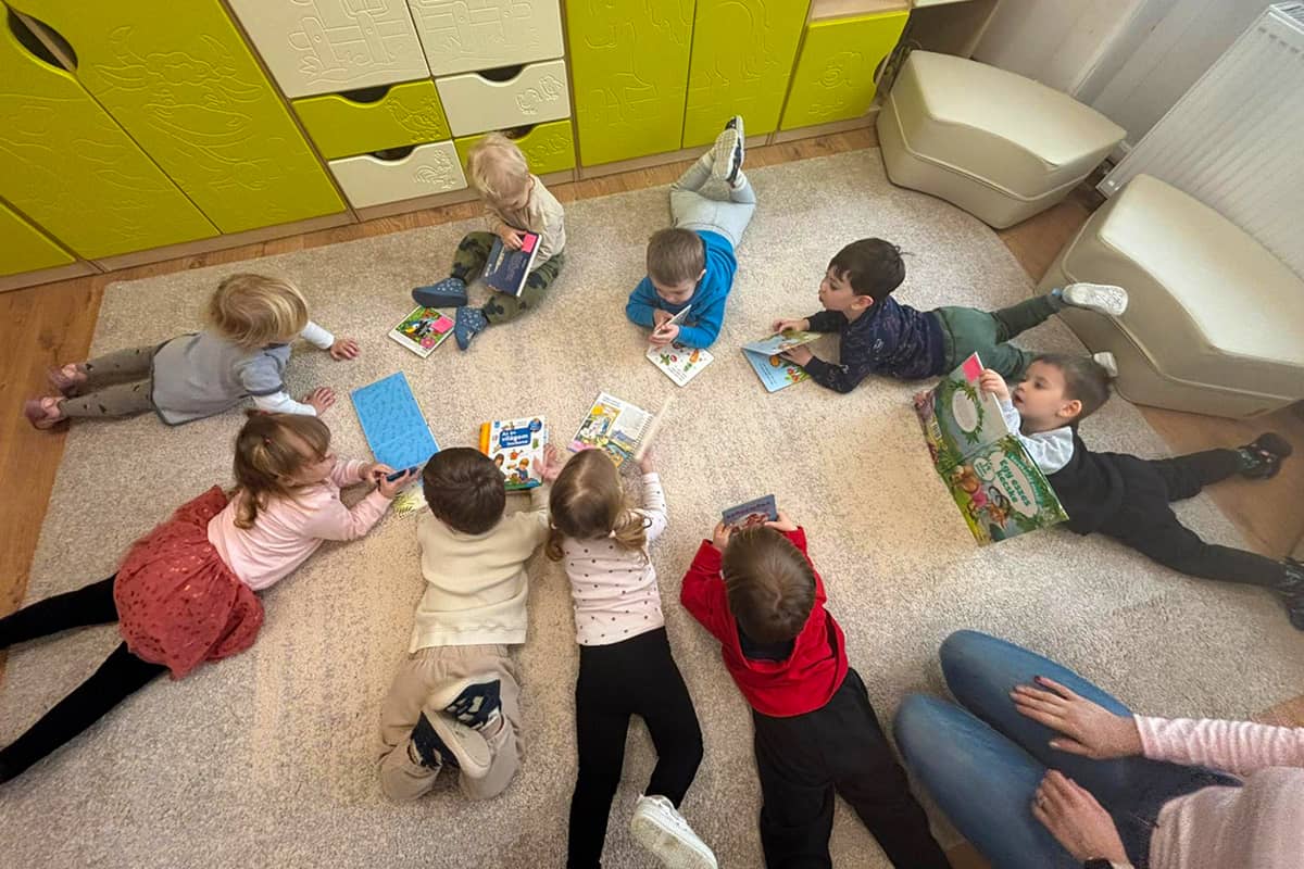Bölcsődés gyermekek hason fekve nézegetik új könyveiket.
