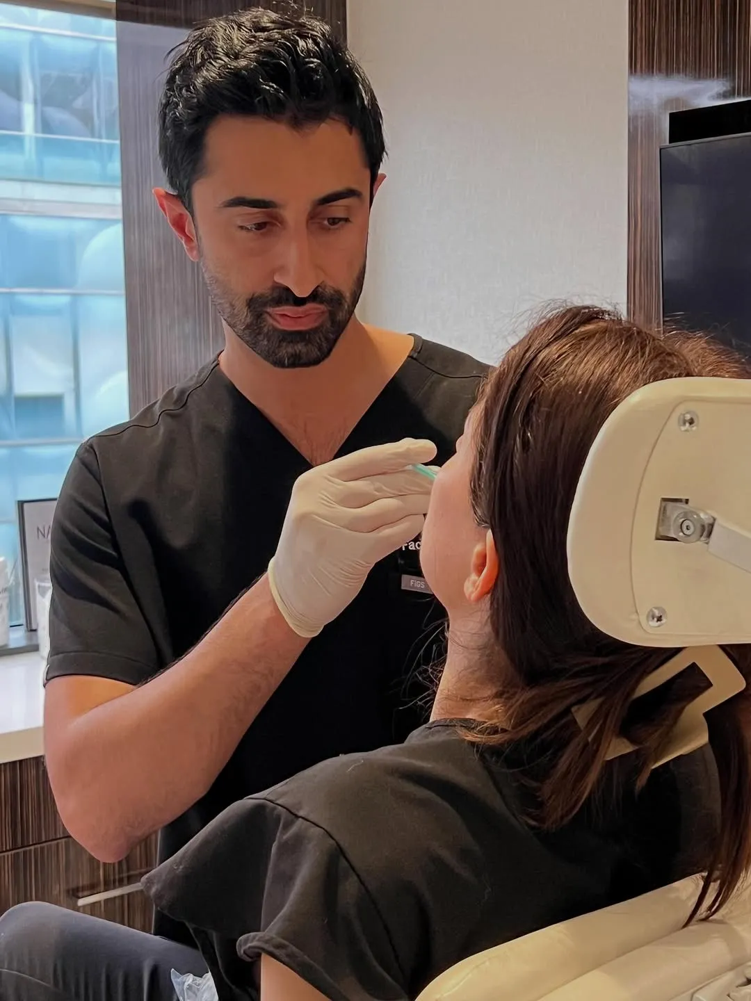 Doctor wearing gloves preparing to administer an injection to a seated female patient in a clinical setting.