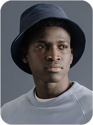 Portrait d’un homme portant un bob bleu marine et un sweat clair, regardant sur le côté avec une expression sérieuse.