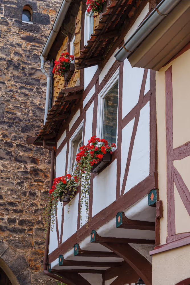 Nahaufnahme eines Fachwerkhaus mit Blumenkästen in den Fenstern das die passende Wohngebäudeversicherung braucht