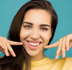 Brunette vrouw met haar handen en vingers wijzend naar haar glimlach voor een blauwe achtergrond