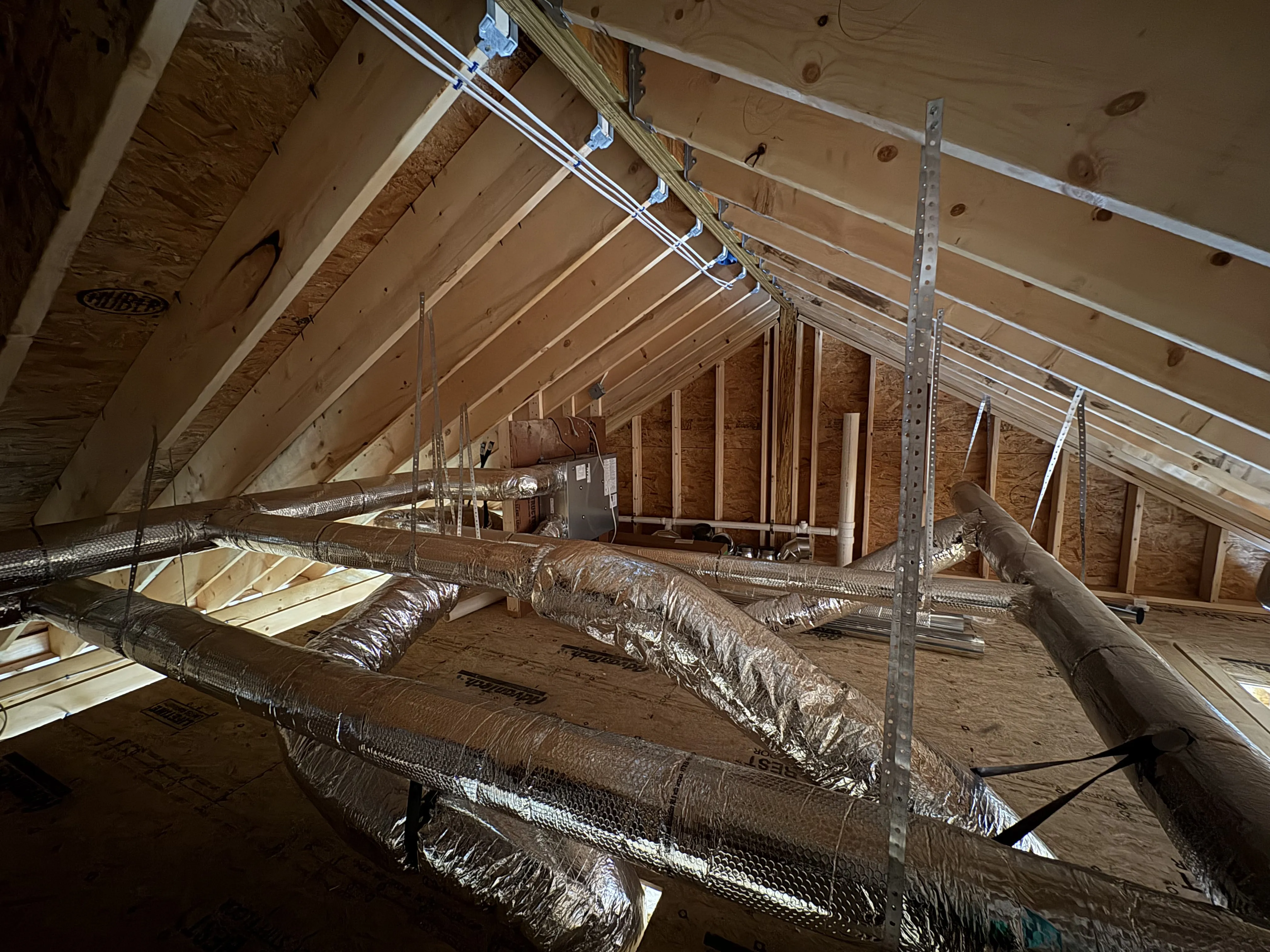 Insulated HVAC ducts installed in an unfinished attic with exposed wooden roof framing.