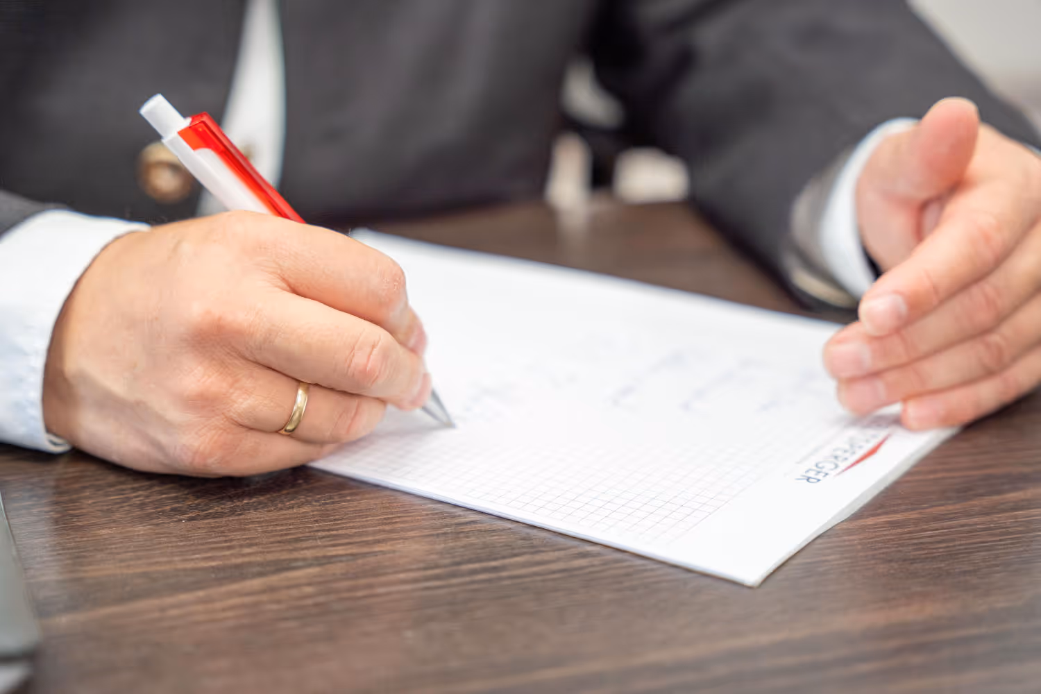 Hand beim Unterschreiben eines Vertrags auf Geschäftspapier von Zeltsperger Immobilien & Wirtschaftsberatung.