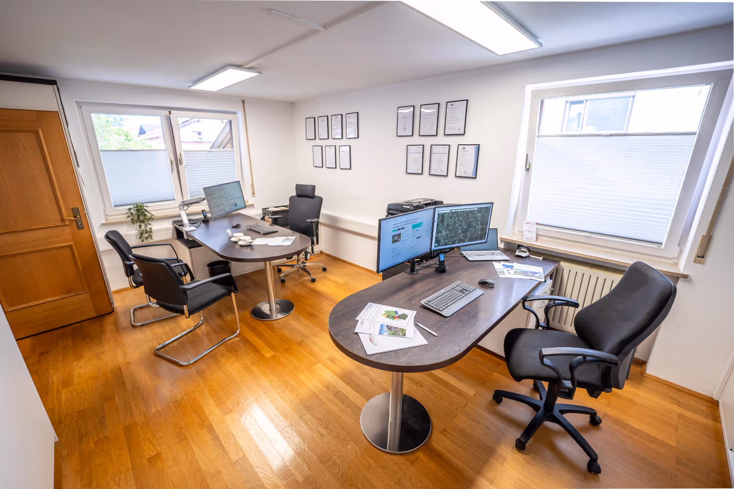 Helles Büro von Zeltsperger Immobilien und Wirtschaftsberatung mit Auszeichnungen an der Wand, braunem Bürotisch und Desktops und Tür mit Regalen.