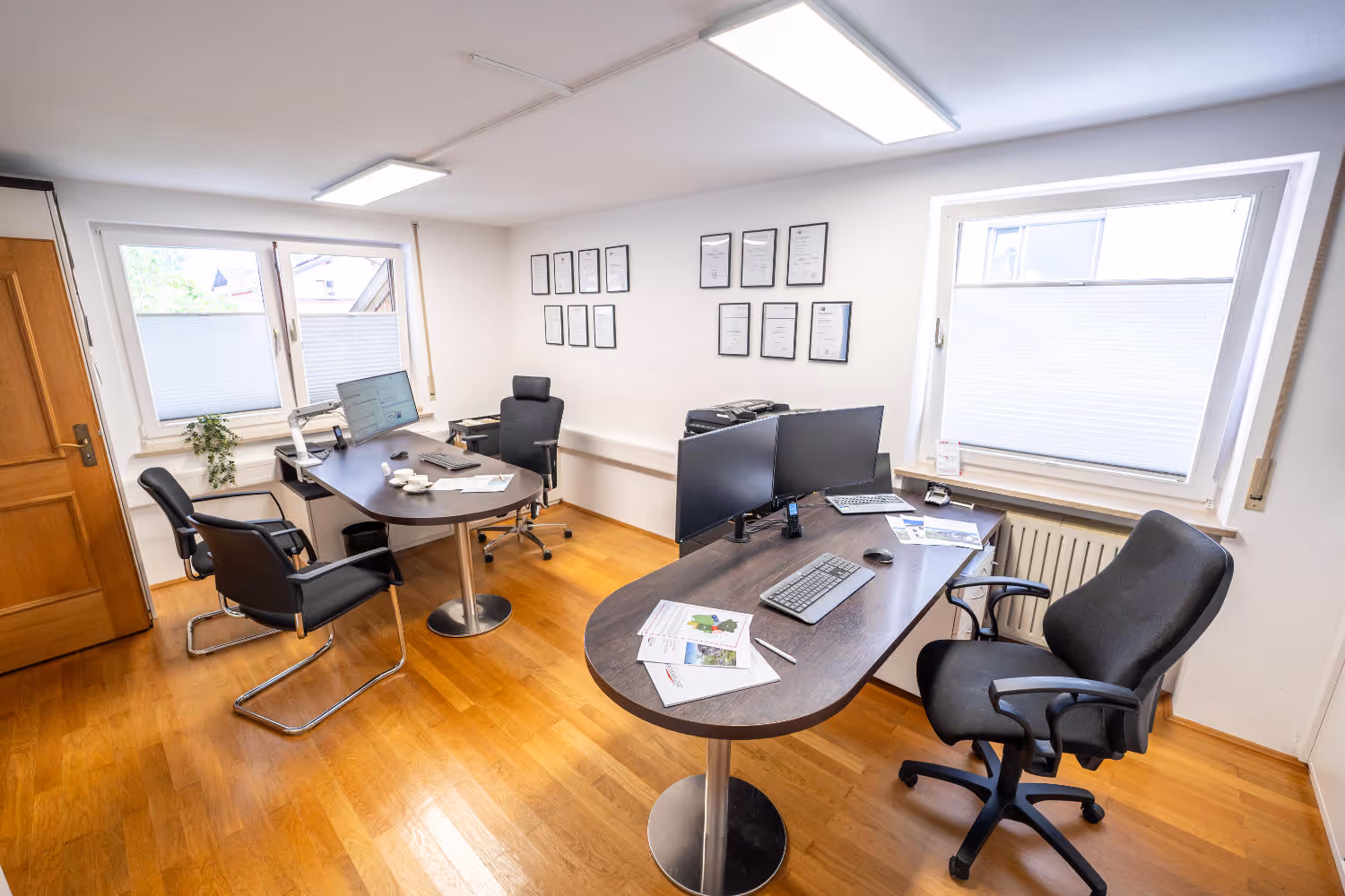 Helles Büro von Zeltsperger Immobilien und Wirtschaftsberatung mit Auszeichnungen an der Wand, braunem Bürotisch und Desktops und Tür mit Regalen.